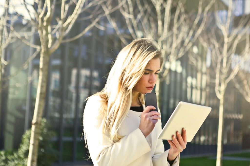 Young female employee using tablet and phone outside | Banded Hours Contract